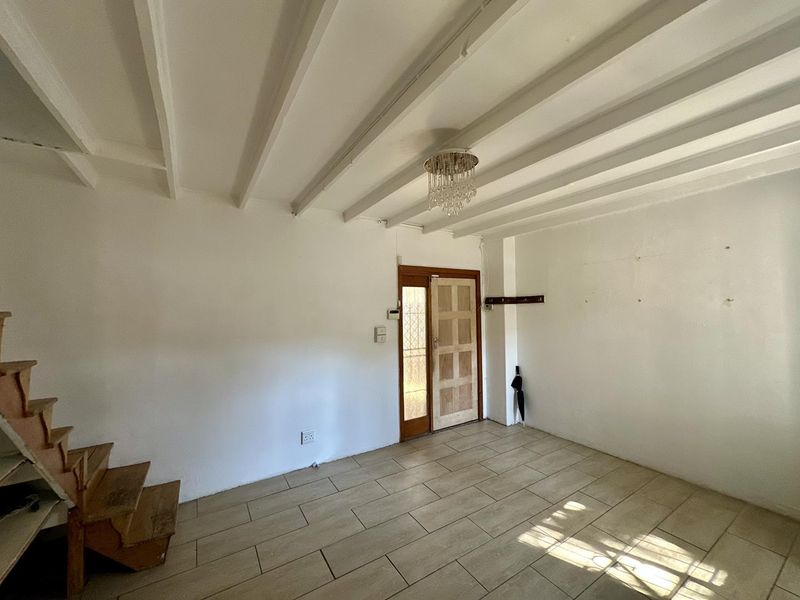 An empty entrance area featuring tiled flooring, exposed ceiling beams, a wooden staircase, and a timber front door with a decorative chandelier.