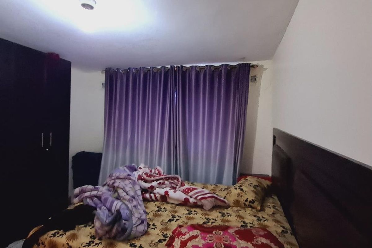 A bedroom featuring a built-in wardrobe and window with curtains, providing a functional sleeping space.