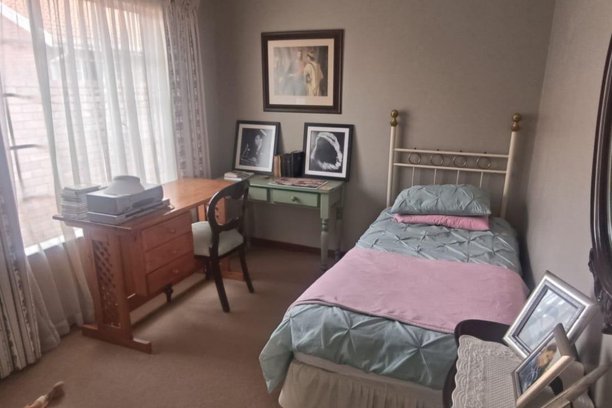 A cozy bedroom featuring neutral wall tones, carpeted flooring, and a large window with curtains, providing a comfortable and functional living space.