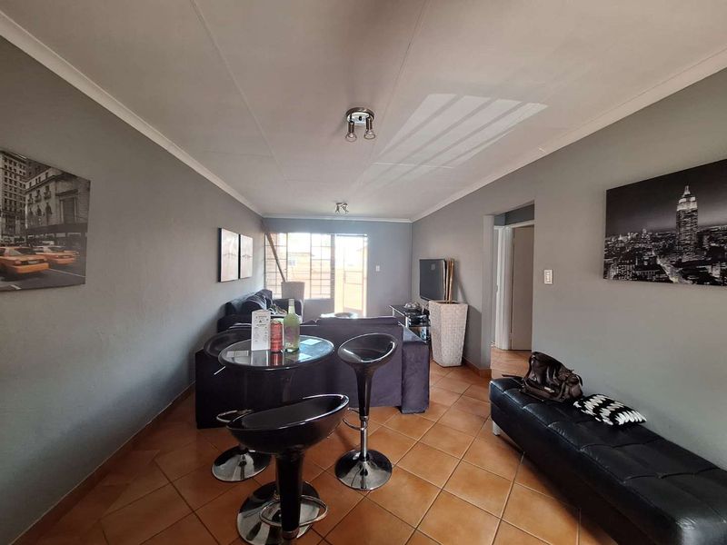 A living room featuring tiled flooring, ceiling coving, and a sliding glass door leading to an outdoor area with a security gate.