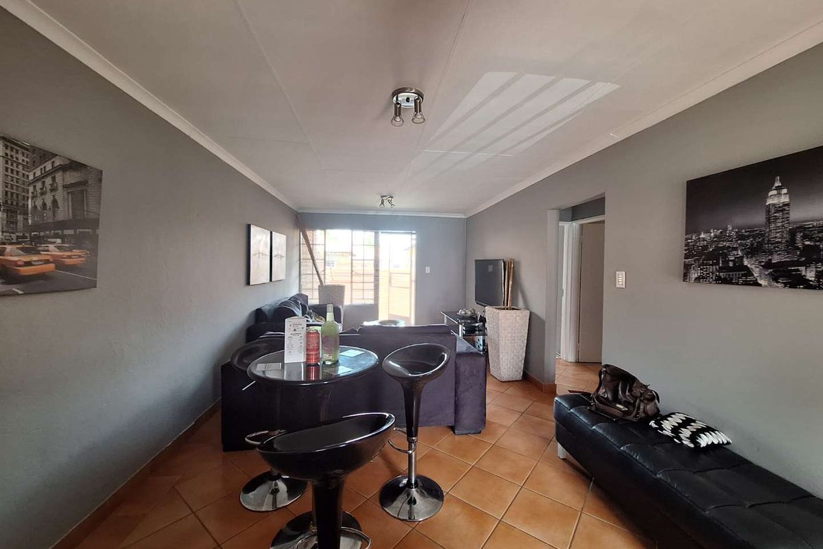 A living room featuring tiled flooring, ceiling coving, and a sliding glass door leading to an outdoor area with a security gate.