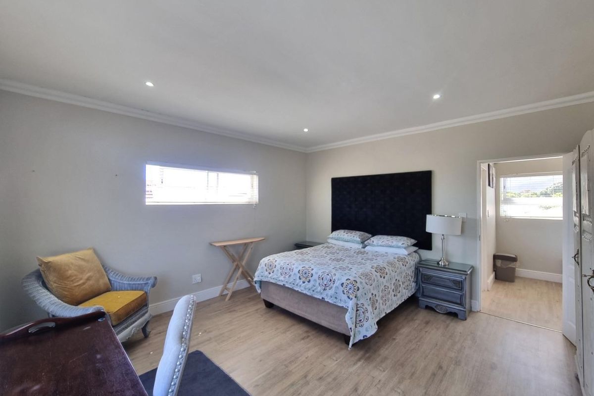 Spacious bedroom featuring light wood-look flooring, recessed ceiling lighting, and a neutral color palette, with an adjoining en-suite bathroom area.