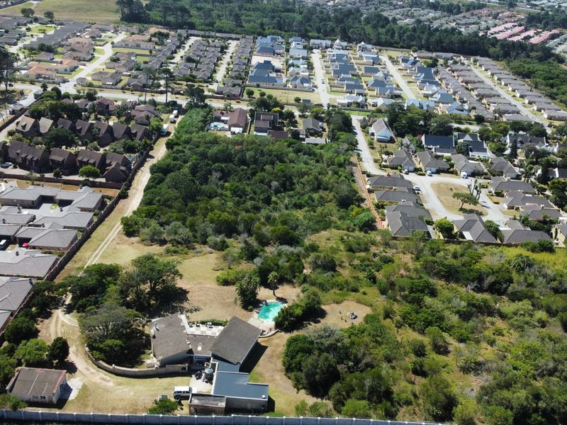 Aerial view of a residential property featuring a swimming pool, surrounded by established vegetation and neighboring suburban housing developments.