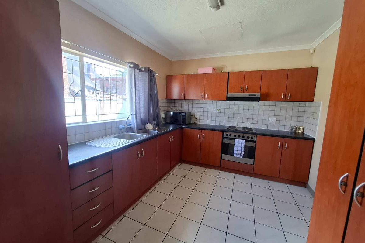 A functional kitchen featuring wood-finish cabinetry, tiled flooring, a built-in oven, hob, and extractor fan with a stainless steel sink.