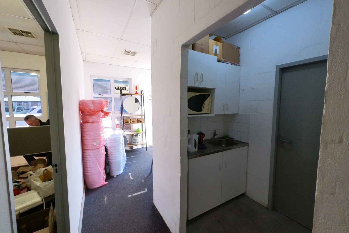 A compact kitchenette area featuring built-in cabinetry, a stainless steel sink, and tiled flooring, adjacent to an office workspace.