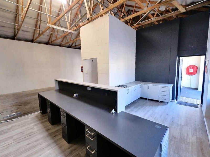 Open-plan industrial workspace featuring exposed timber roof trusses, a built-in reception desk, fitted cabinetry, and durable laminate flooring.