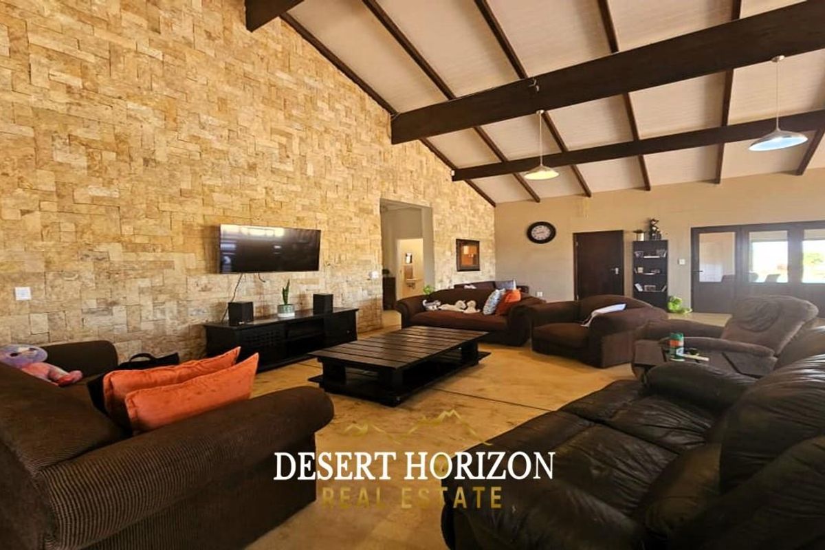 Spacious living area featuring a striking natural stone feature wall, vaulted ceilings with exposed timber beams, and polished concrete flooring.
