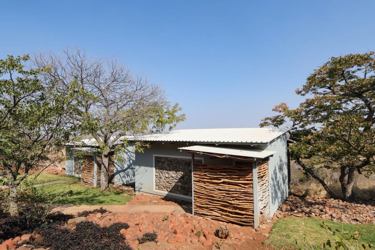 Exterior view of a lodge unit featuring corrugated metal roofing, stone masonry accents, and rustic timber cladding set within a natural landscape.