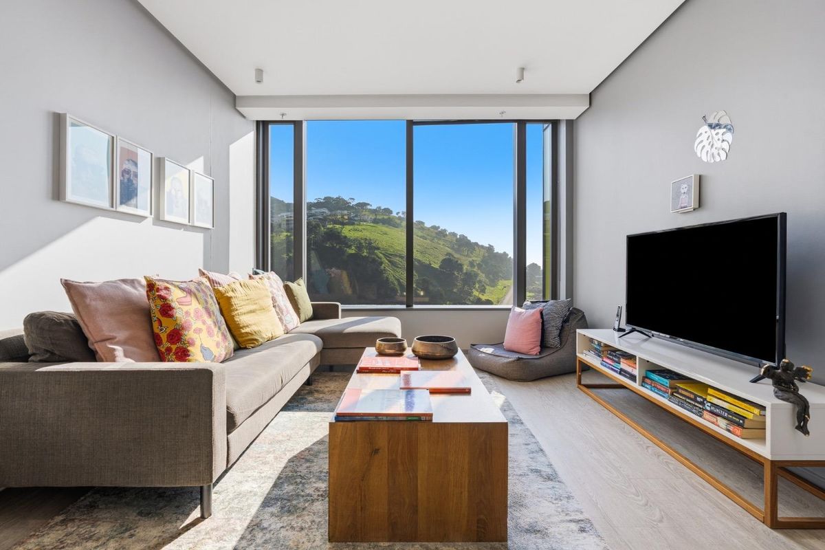 Modern living room featuring floor-to-ceiling windows with scenic hillside views, neutral walls, and light-toned laminate flooring.