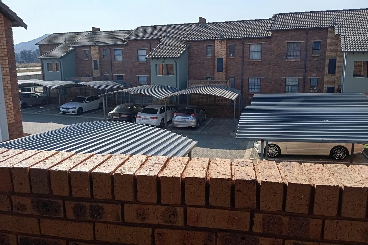 View of the apartment complex rear elevation featuring brick facade, tiled roofing, and multiple covered parking bays.