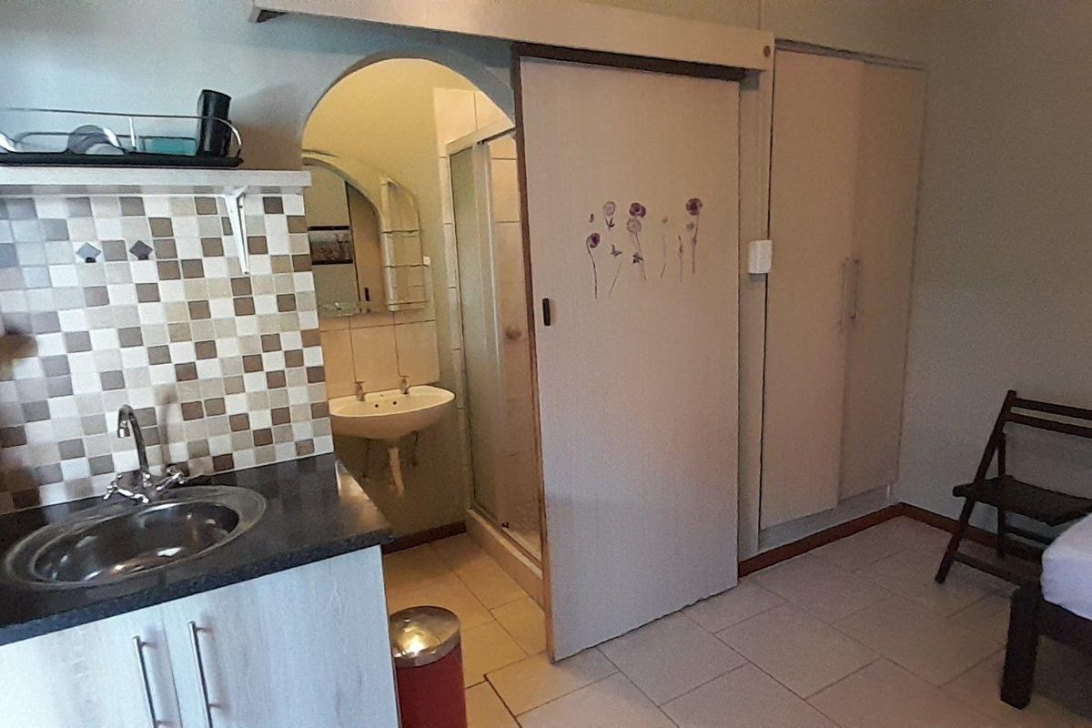 Compact open-plan studio apartment featuring a kitchenette with tiled backsplash, built-in storage, and an en-suite bathroom with a shower and pedestal basin.