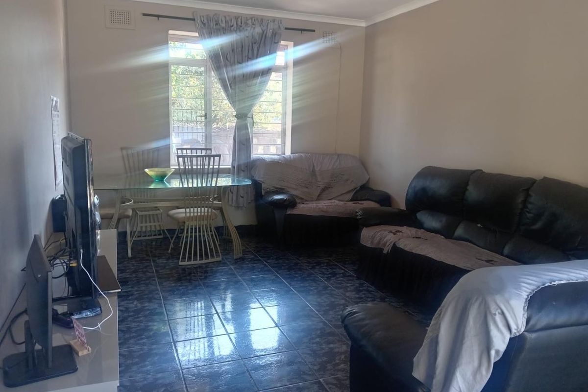 A living room area featuring tiled flooring, natural light through a window with security bars, and standard ceiling cornicing.