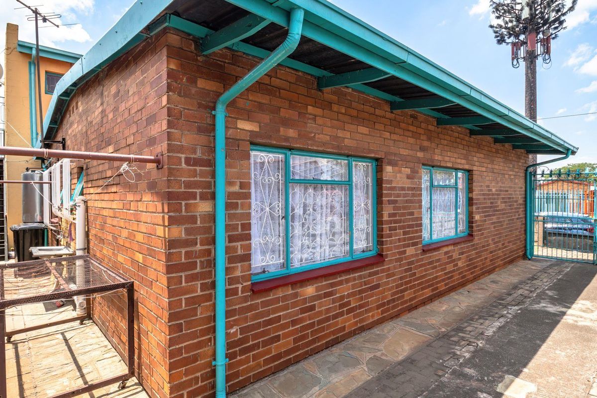 Exterior view of the rear brick facade featuring metal window frames, guttering, and paved walkway area.