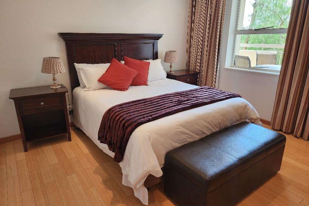 A well-maintained bedroom featuring laminate flooring, a large window providing natural light, and direct access to an outdoor balcony area.