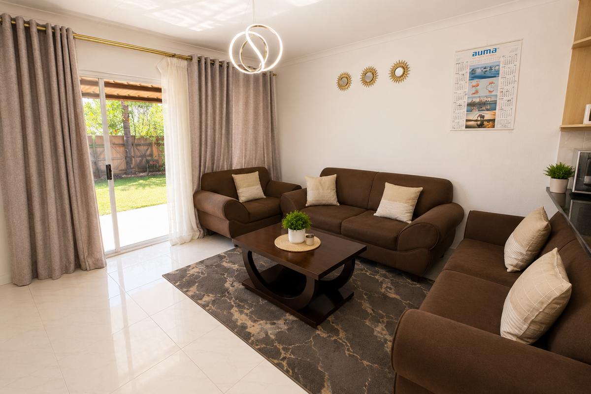 A bright living room featuring large sliding glass doors leading to the garden, neutral tiled flooring, and a contemporary pendant light fixture.