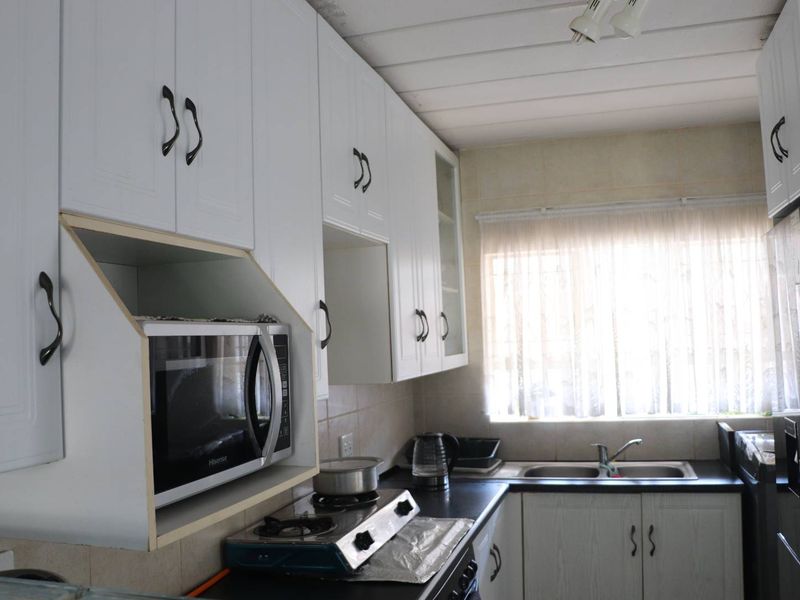 A functional kitchen featuring white cabinetry, dark countertops, a double basin sink, and a dedicated built-in microwave shelf.
