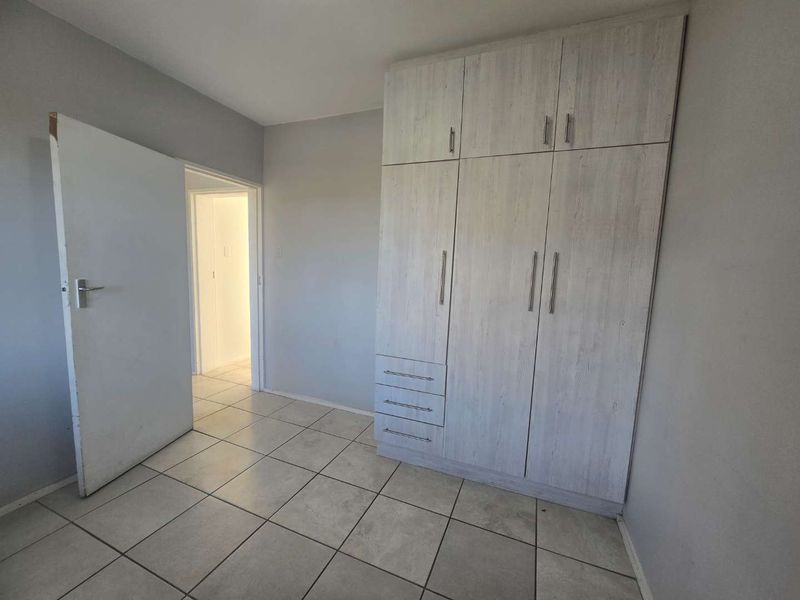 A clean, empty bedroom featuring light-toned built-in wardrobes and neutral tiled flooring, offering a versatile space ready for personalization.