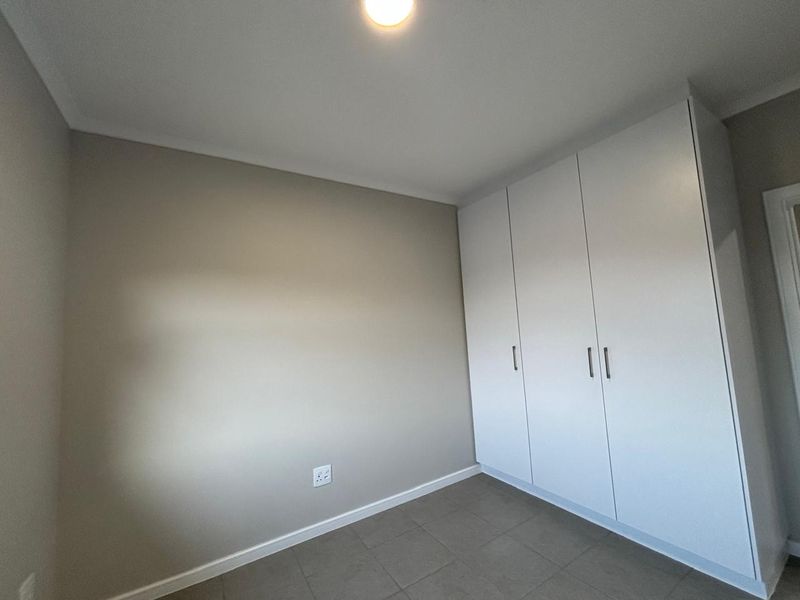 A clean, empty bedroom featuring neutral wall tones, tiled flooring, and ample built-in cupboard storage.