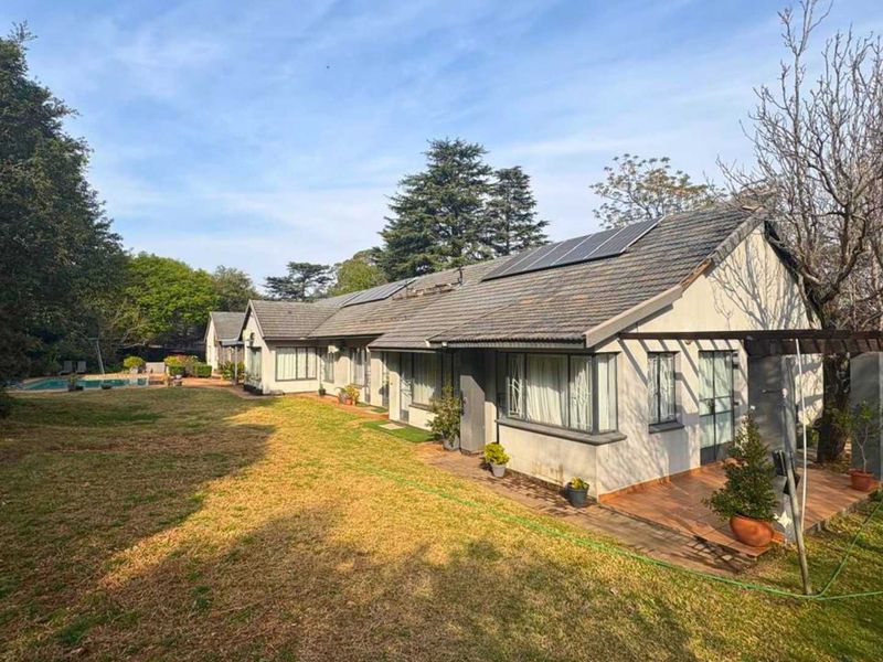 Rear view of the property featuring a tiled roof with solar panels, a covered patio area, and a swimming pool set in a spacious garden.