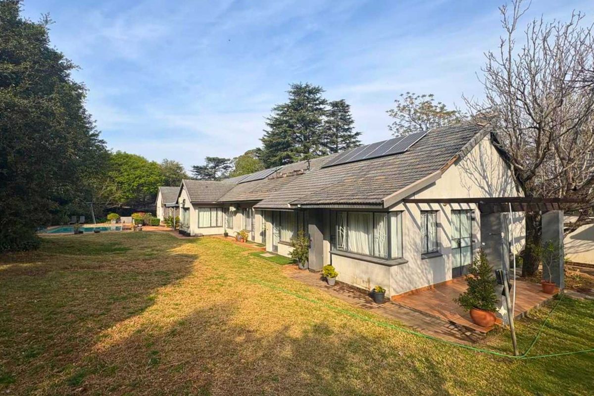 Rear view of the property featuring a tiled roof with solar panels, a covered patio area, and a swimming pool set in a spacious garden.