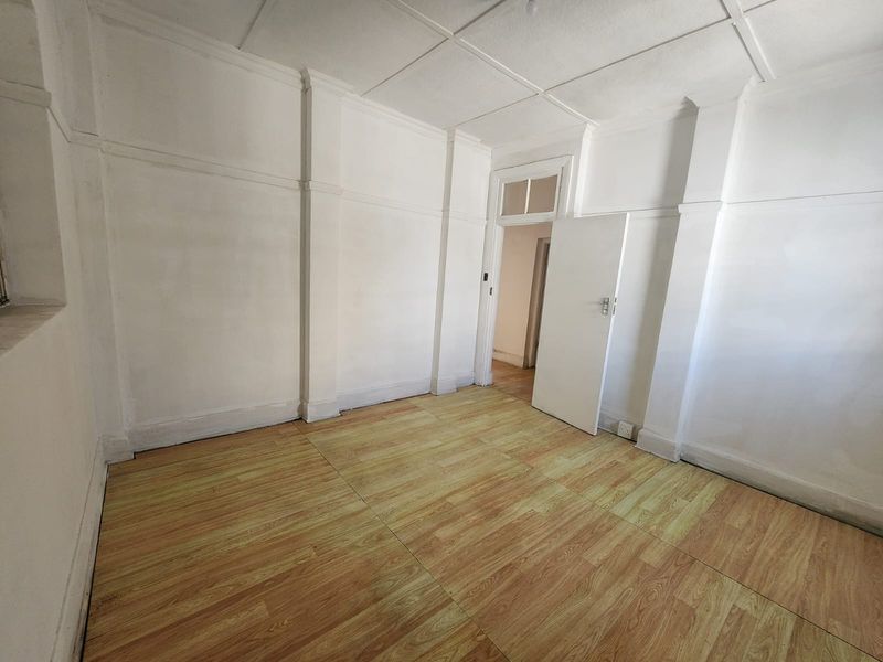 An empty bedroom featuring laminate flooring, white walls, and a panelled ceiling, offering a blank canvas for renovation or interior design.