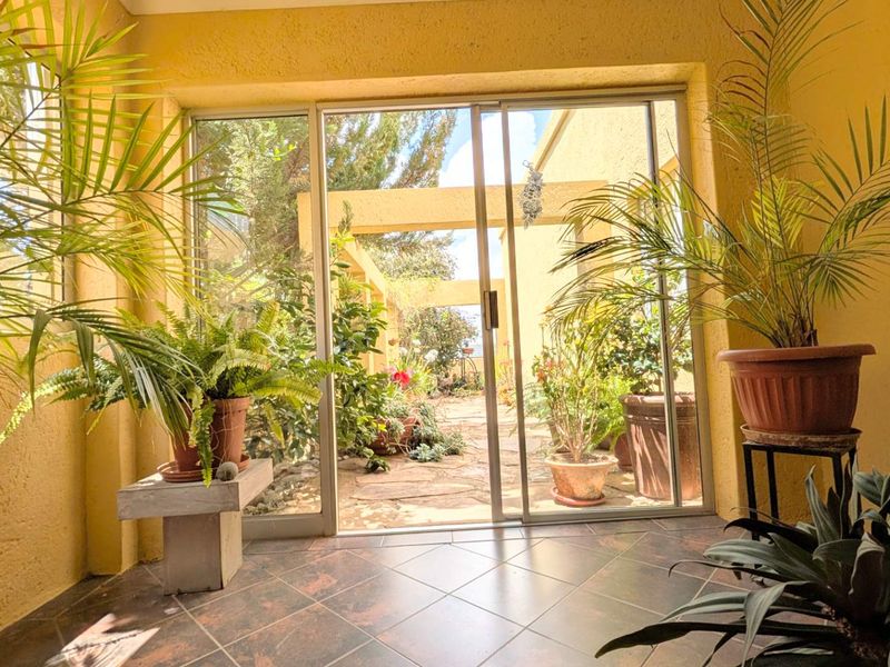 A sunlit enclosed patio area featuring tiled flooring and large sliding glass doors that provide direct access to the outdoor garden space.