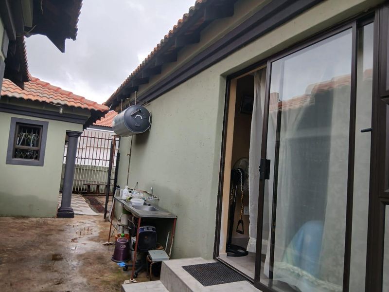Exterior view of the side courtyard featuring a wall-mounted geyser, stainless steel utility sink, and sliding glass door access to the interior.