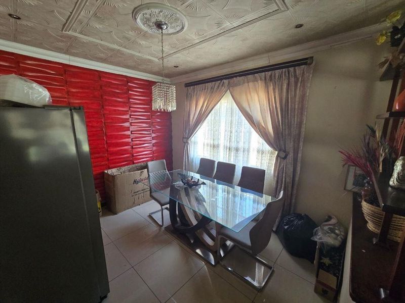 Dining room featuring tiled flooring, a decorative ceiling rose with textured ceiling tiles, and a prominent red feature wall.