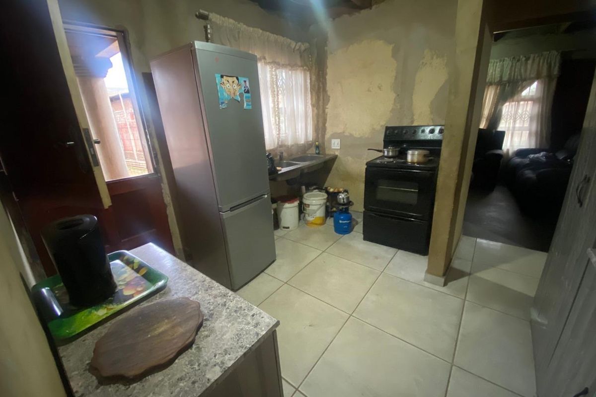 A basic kitchen area featuring tiled flooring, a freestanding stove, and a sink, requiring significant renovation and wall finishing to improve the space.