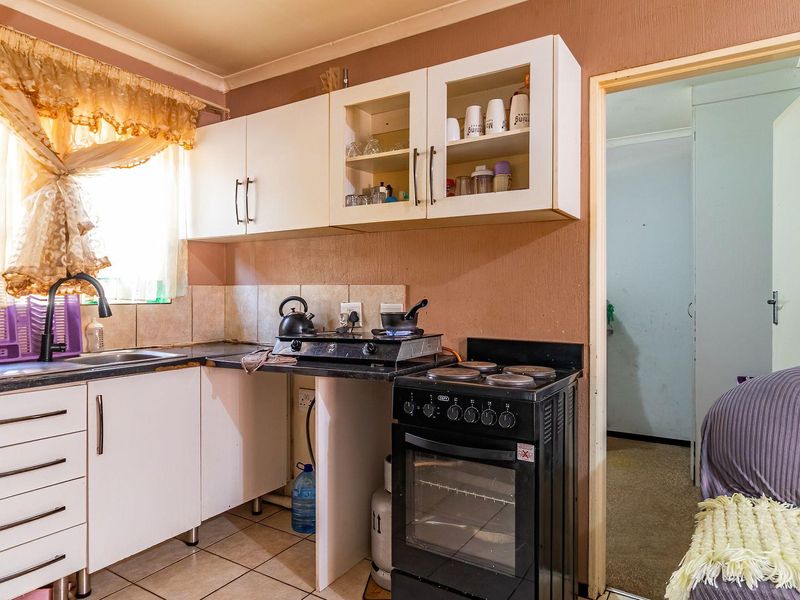 A compact kitchen featuring built-in cabinetry, a tiled backsplash, and a freestanding stove, offering a functional layout with potential for modern updates.
