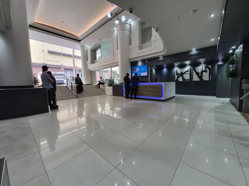 Modern office building lobby featuring a reception desk, high ceilings with recessed lighting, and polished tiled flooring.