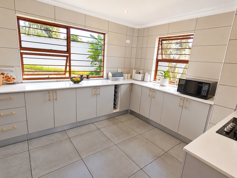 Modern kitchen featuring light grey cabinetry, stone countertops, large format floor tiles, and integrated appliances with a clean, contemporary finish.