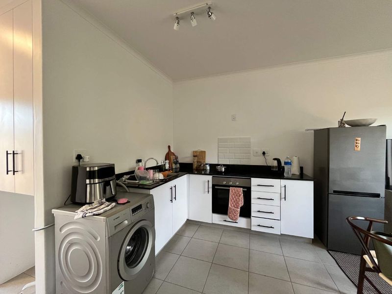 A functional kitchen featuring white cabinetry, dark stone countertops, subway tile splashback, and integrated oven, with tiled flooring throughout.