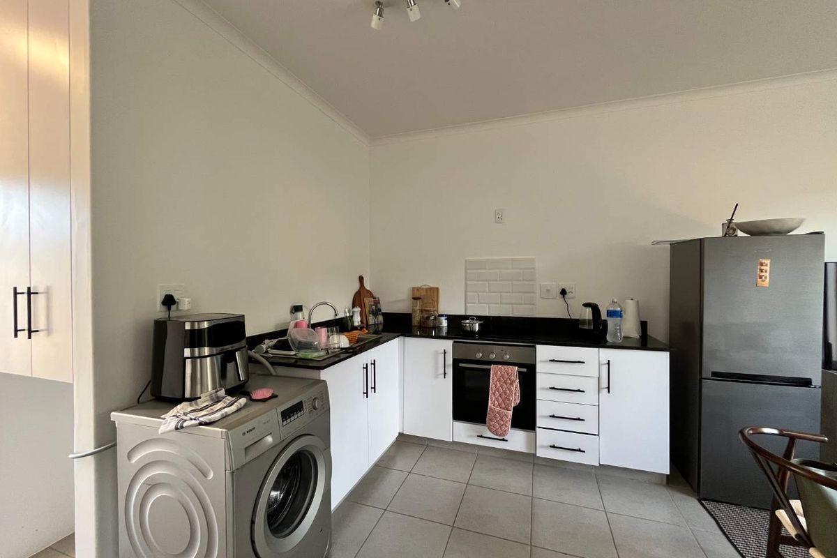 A functional kitchen featuring white cabinetry, dark stone countertops, subway tile splashback, and integrated oven, with tiled flooring throughout.