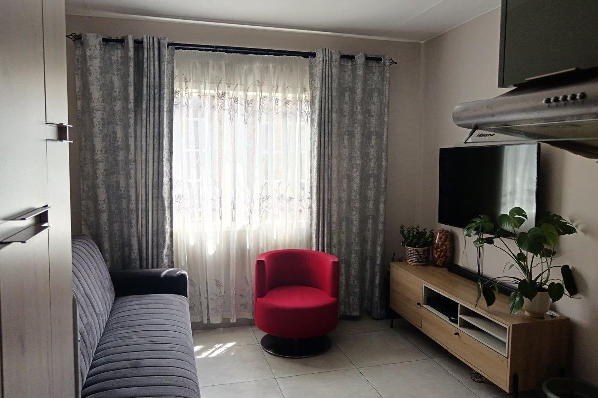 A compact living room featuring tiled flooring and a window with curtain treatments, providing a functional and comfortable space.