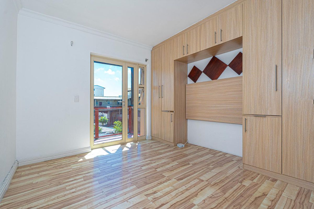 A bright bedroom featuring light wood-look flooring, extensive built-in cabinetry, and a glass door providing access to a private balcony.