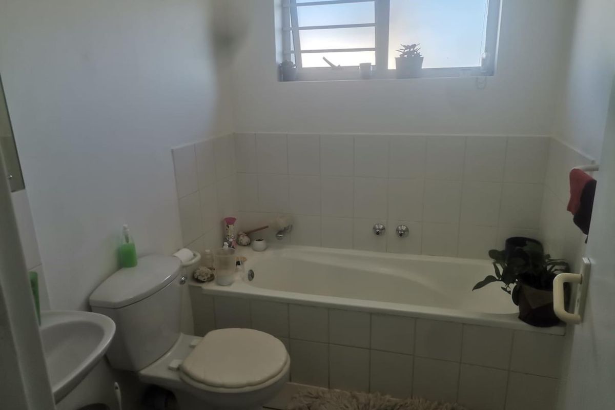 A functional bathroom featuring a built-in bathtub, white ceramic wall tiling, a standard toilet, and a pedestal basin with a louvered window.