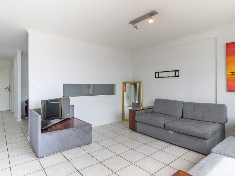 A bright living room featuring ceramic floor tiles, recessed ceiling lighting, and a unique internal window, offering a clean and functional space.