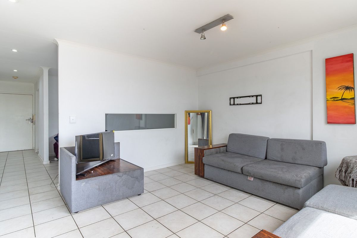 A bright living room featuring ceramic floor tiles, recessed ceiling lighting, and a unique internal window, offering a clean and functional space.
