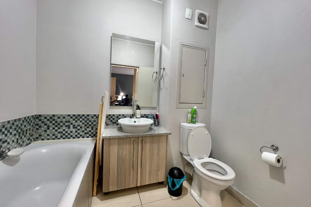 A functional bathroom featuring a bathtub, a vanity with a vessel sink, a toilet, and a wall-mounted extractor fan.