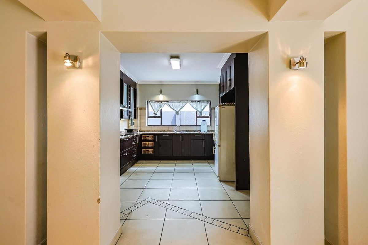 A view through a wide doorway into a functional kitchen featuring dark wood cabinetry, tiled flooring, and integrated lighting.