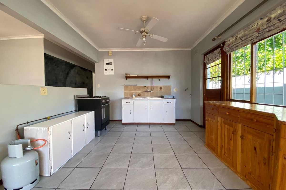 A functional kitchen featuring tiled flooring, built-in cabinetry, a gas stove, and direct access to the exterior via a timber door.