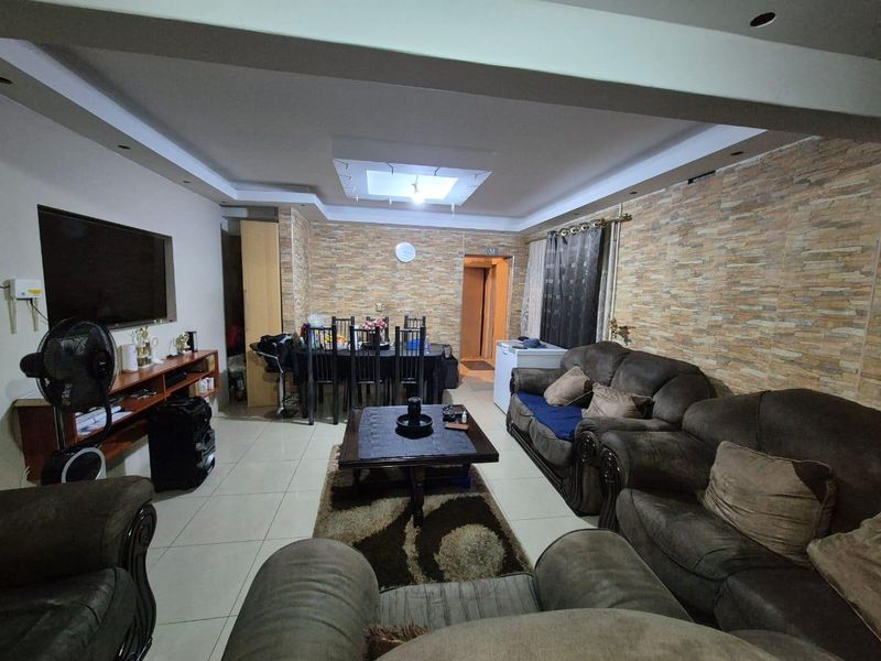 Spacious open-plan living and dining area featuring a stone veneer feature wall, recessed ceiling with cove lighting, and neutral tiled flooring throughout.