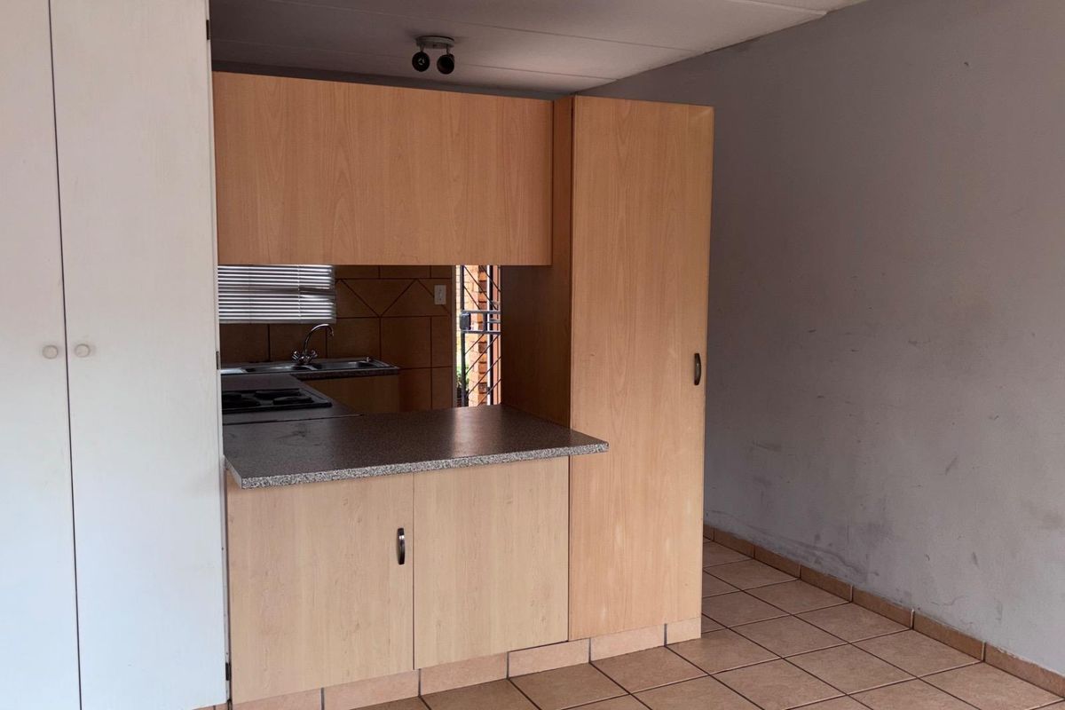 A compact kitchen area featuring light wood-look cabinetry, a built-in hob, and tiled flooring, currently in need of cosmetic updates.