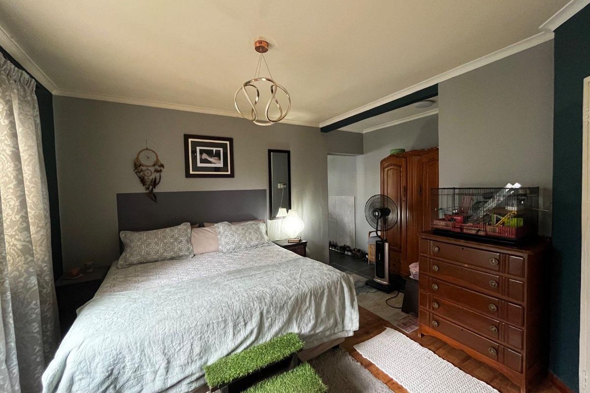 A well-proportioned bedroom featuring neutral grey walls, crown molding, and warm timber flooring, offering a comfortable and functional living space.