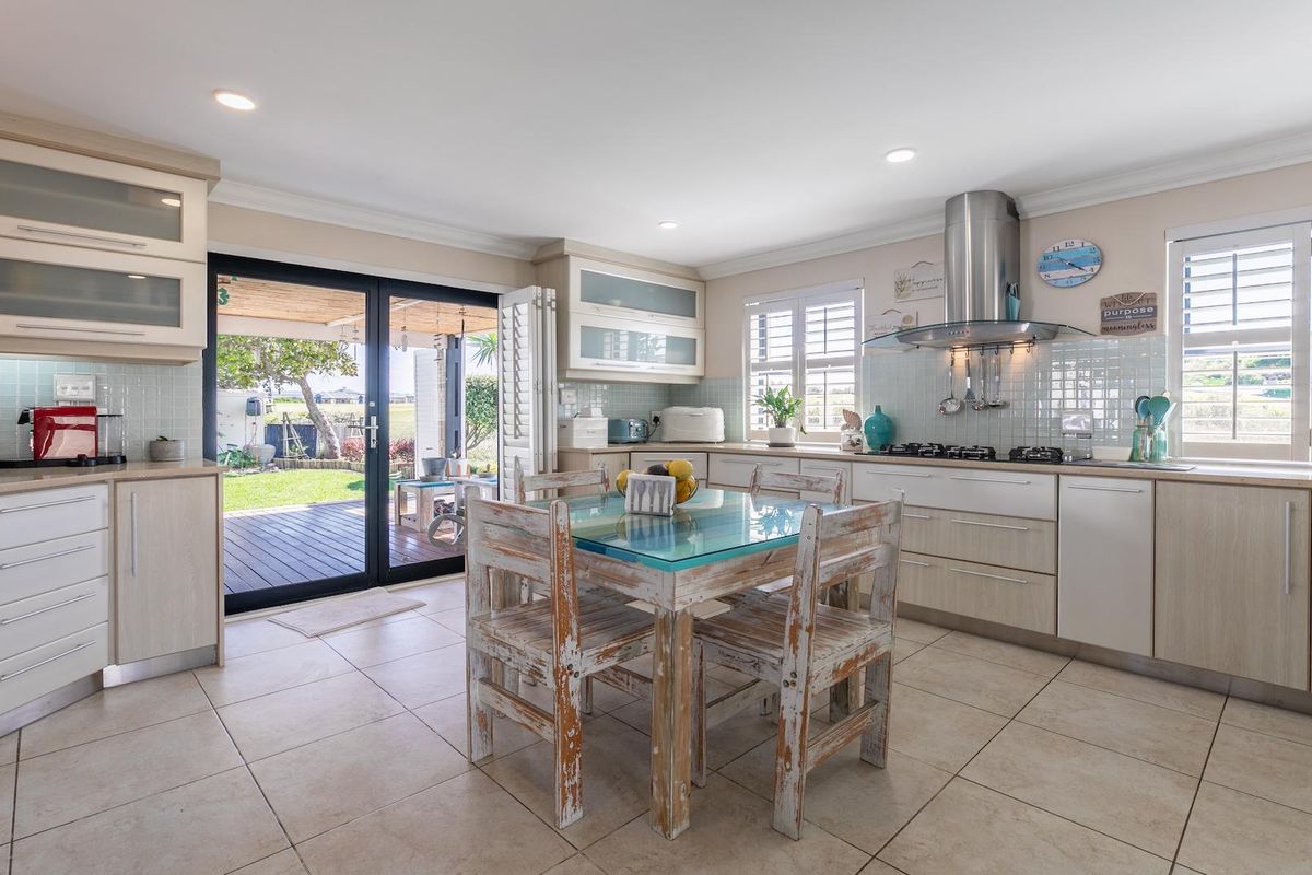 A bright, modern kitchen featuring light wood cabinetry, tiled backsplash, stainless steel extractor fan, and direct access to an outdoor patio area.