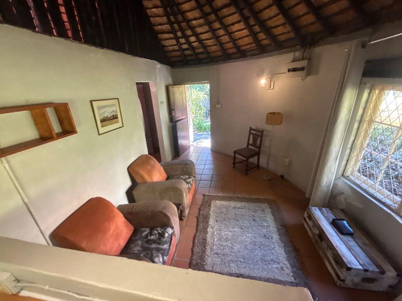 A cozy living room in a cottage featuring a traditional thatched roof with exposed rafters, terracotta tiled flooring, and diamond-pattern security window bars.