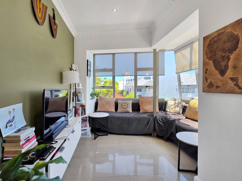 A bright living room featuring large windows, tiled flooring, and decorative ceiling cornices, offering a comfortable and well-lit space.