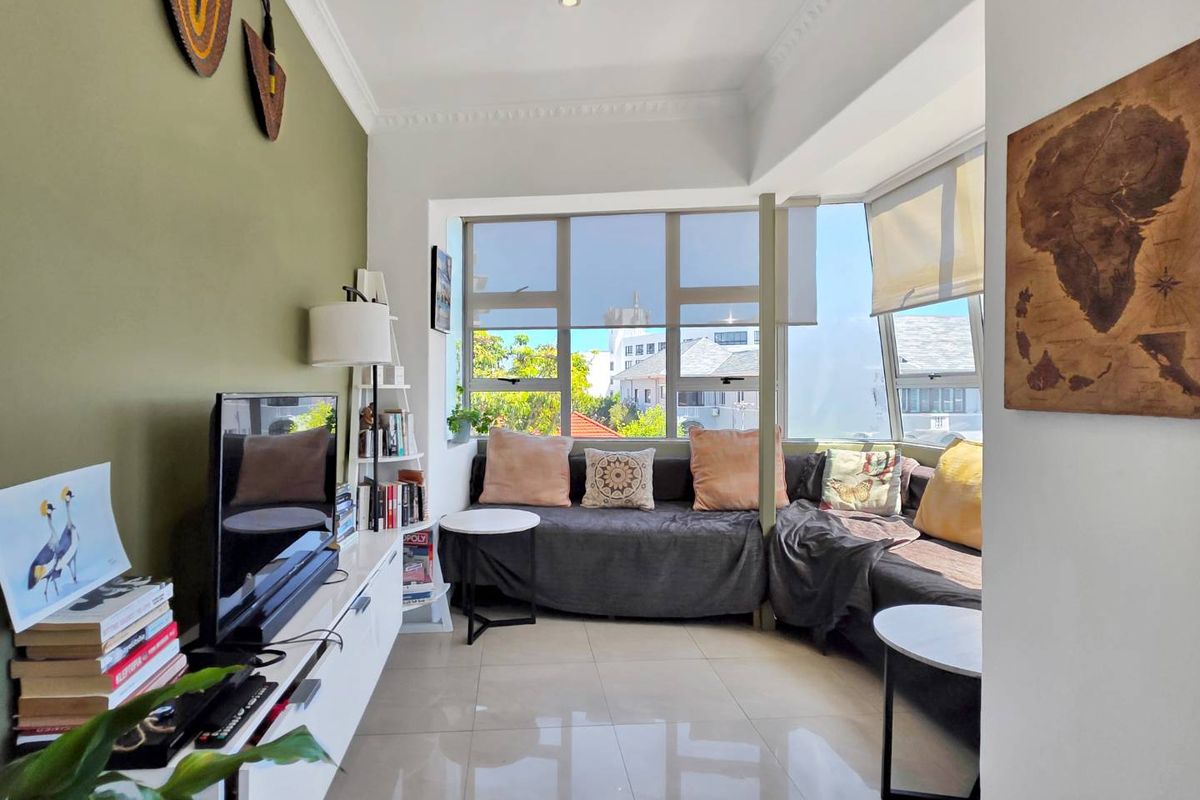 A bright living room featuring large windows, tiled flooring, and decorative ceiling cornices, offering a comfortable and well-lit space.