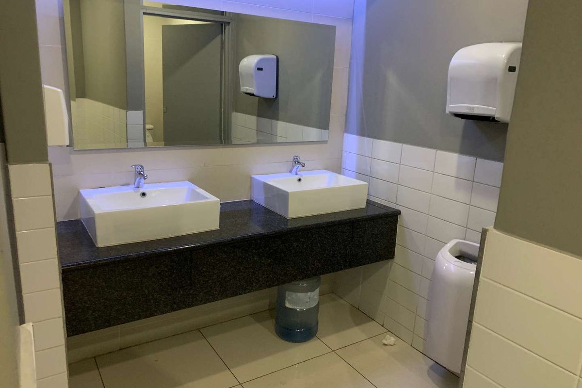 A clean commercial office restroom featuring a double vanity with granite countertop, white ceramic basins, and wall-mounted paper towel dispensers.